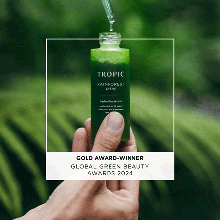 Hand holding Tropic Rainforest Dew hydration serum bottle with a dropper above it, featuring text “Gold Award-Winner, Global Green Beauty Awards 2024.” There are the following quotes: